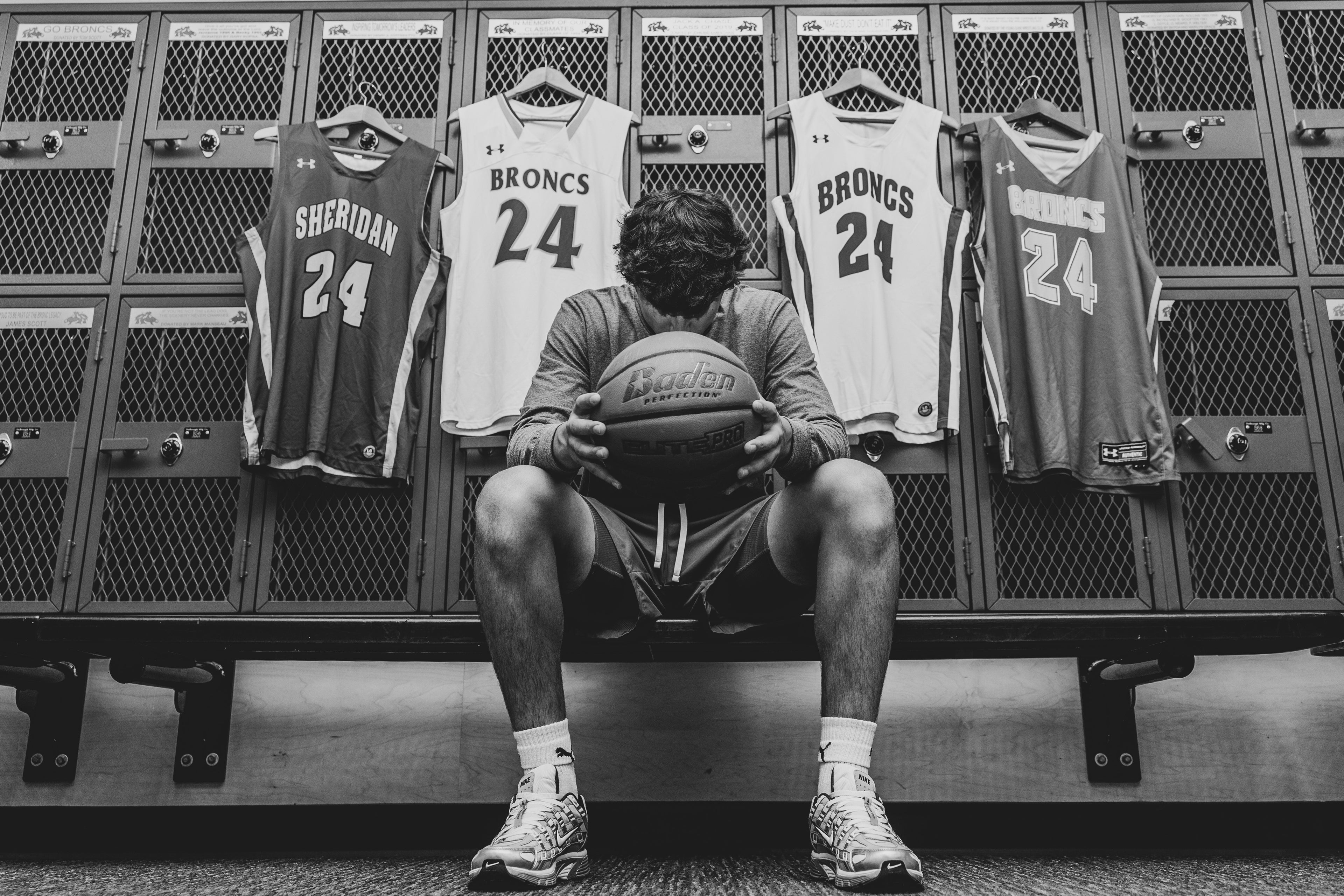 Person sitting in a locker room with basketball jerseys hanging on lockers